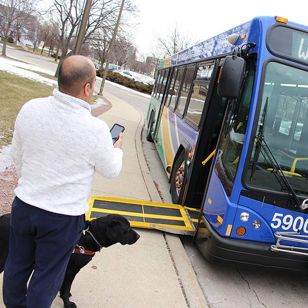 Man holding phone with service dog near bus